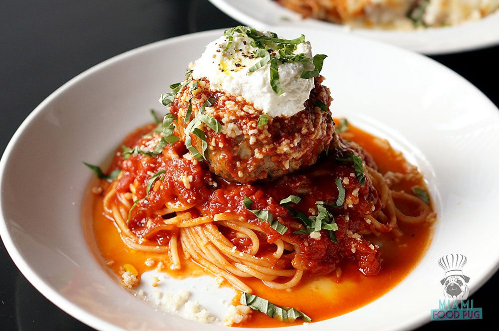 a plate of spaghetti with a meatball and parmesan cheese