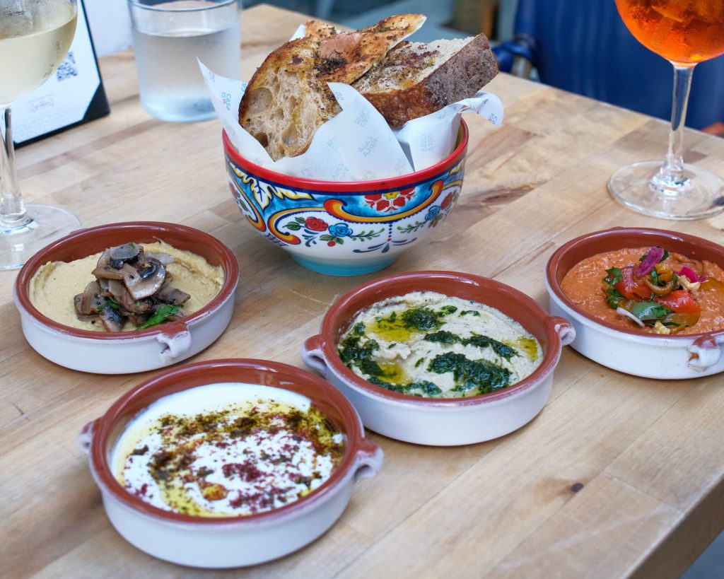 a table with four bowls of dip and a basket of bread