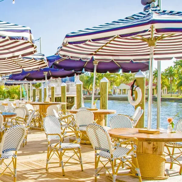 A waterfront dining area with tables, chairs, and umbrellas.