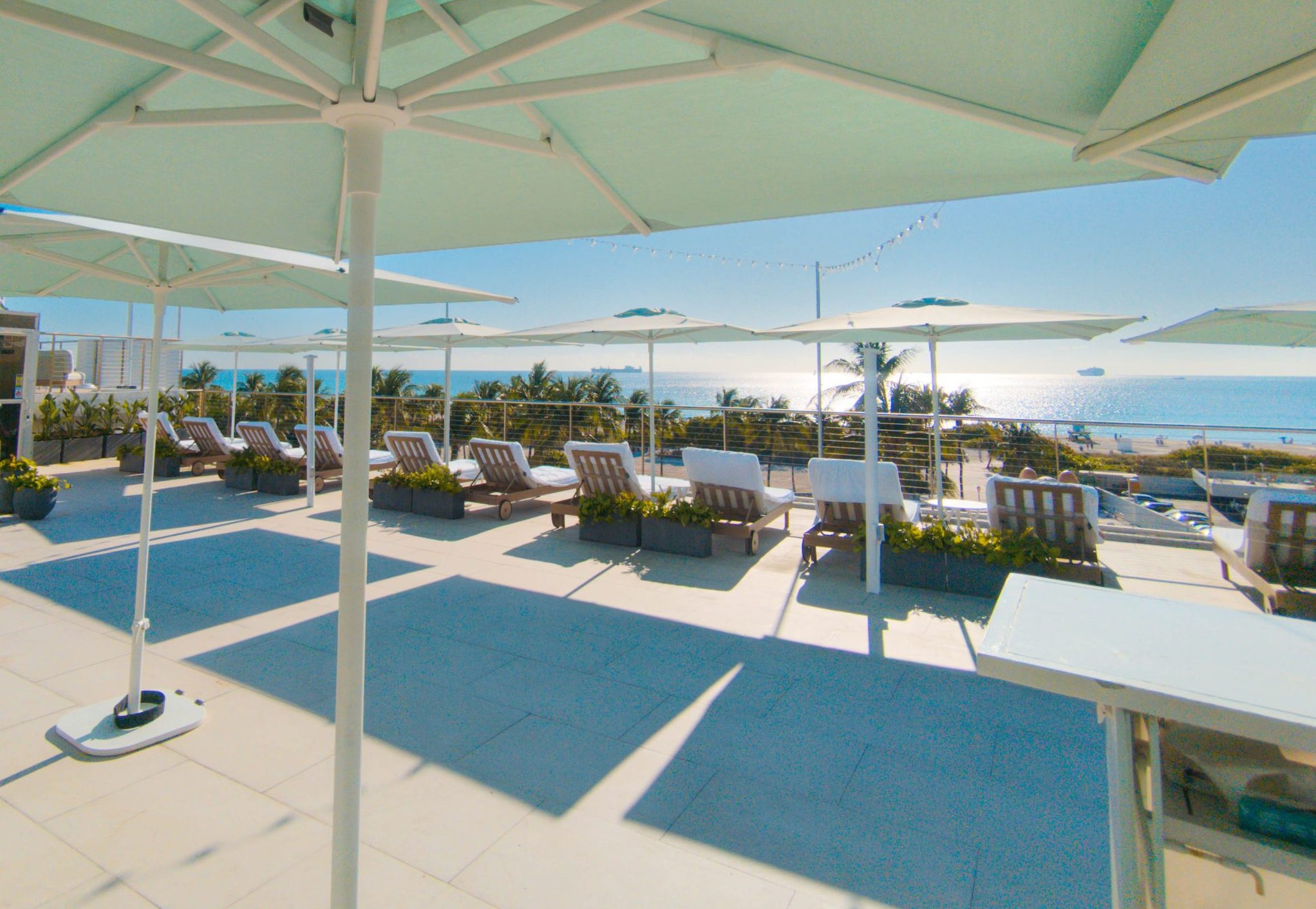 A pool area with lounge chairs and umbrellas overlooking the ocean